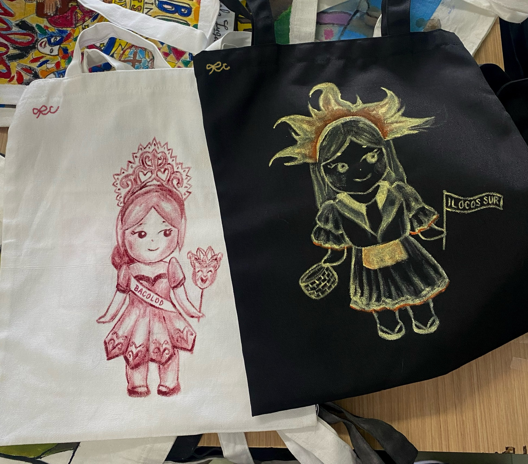 Two tote bag illustrations, one red character and one dark green character.