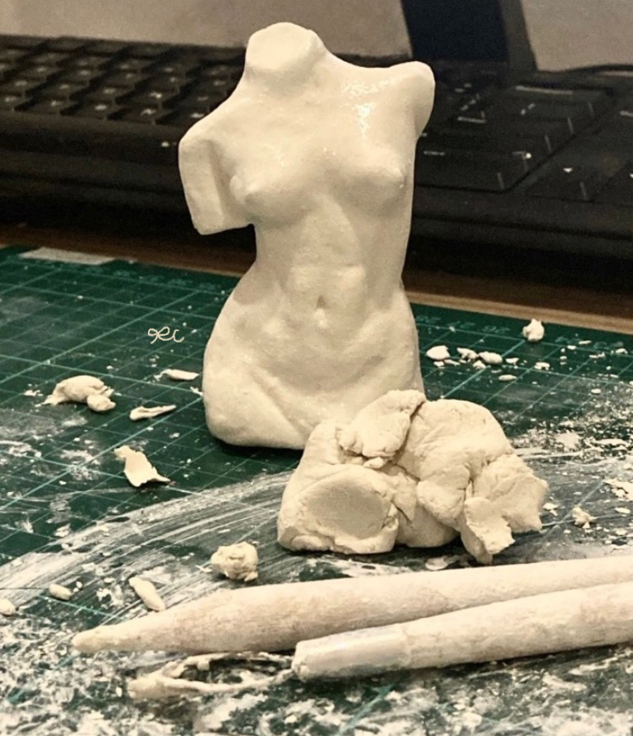 Small pale clay torso sculpture standing on a work surface.