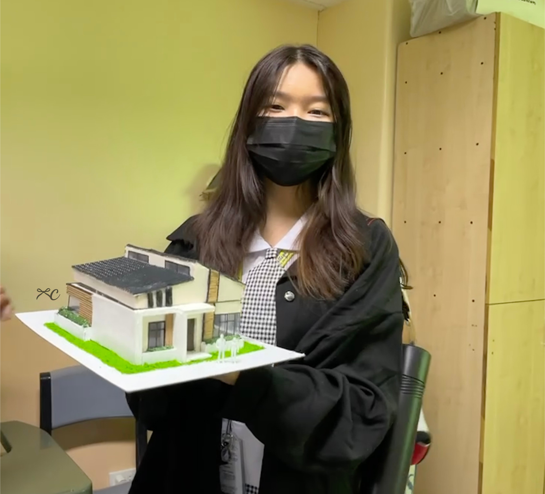 A person holding a white-and-green house scale model on a black base.