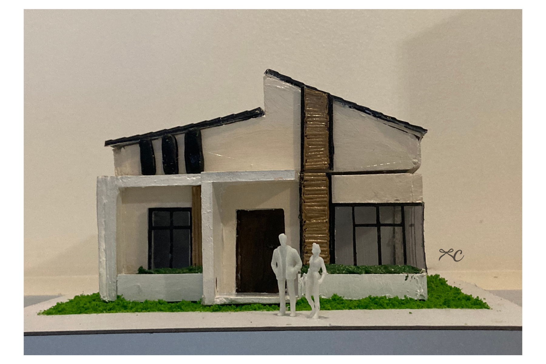 Front view of a white and timber house scale model with lawn and small figures.