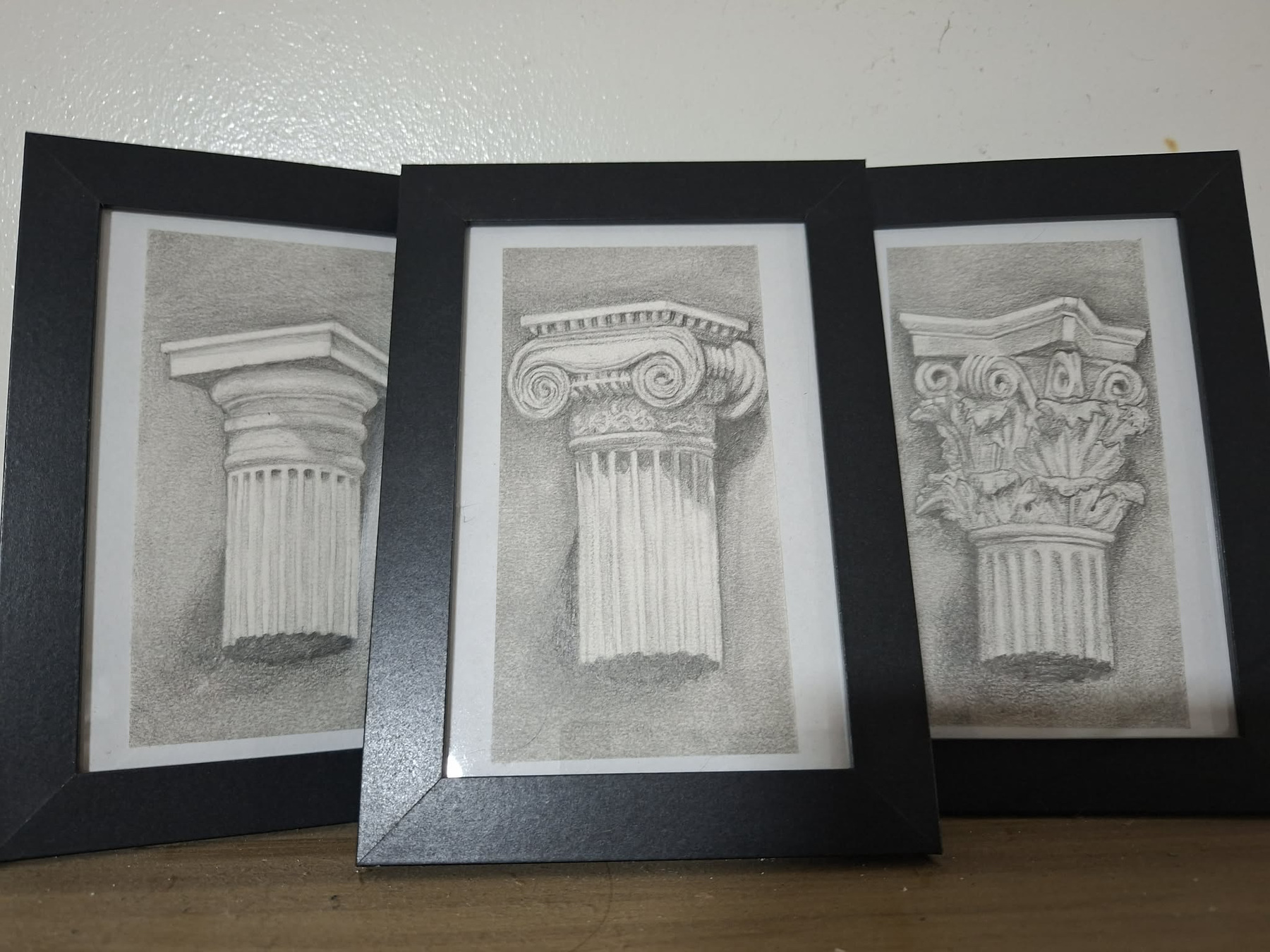 Photograph of three framed graphite studies of classical column capitals.